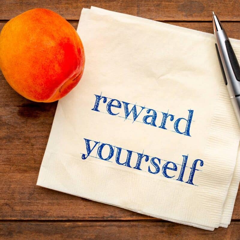 image of reward yourself written on a napkin on a brown table with a pen on the side